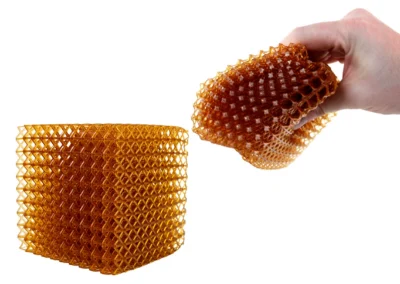 Der durchsichtige Gitterwürfel „Elastic DL160“ wird von Hand gebogen, wodurch die Elastomerflexibilität und die Druckfestigkeit demonstriert werden